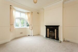 A largely cream-painted room is carpeted and has cream drapes. A replica fireplace sits against one wall.